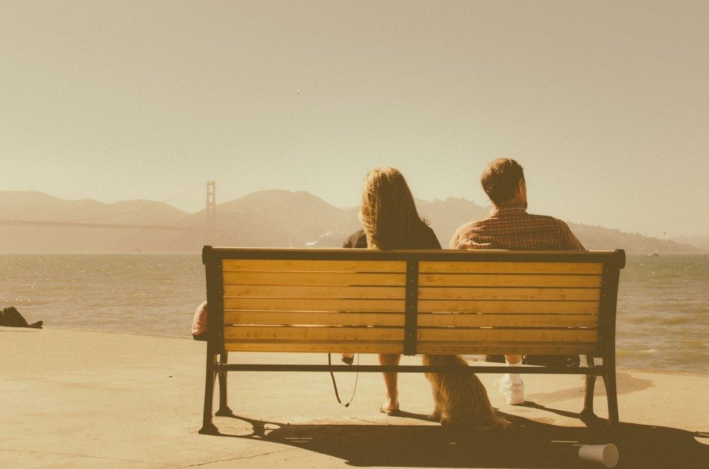 A couple site on a park bench looking out over San Francisco Bay.