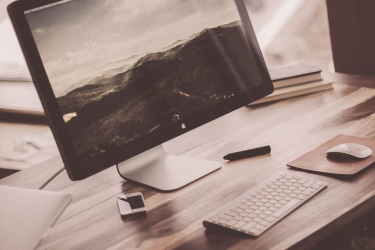 A nice, clean office desk with an Apple monitor, keyboard, mouse and iPhone.